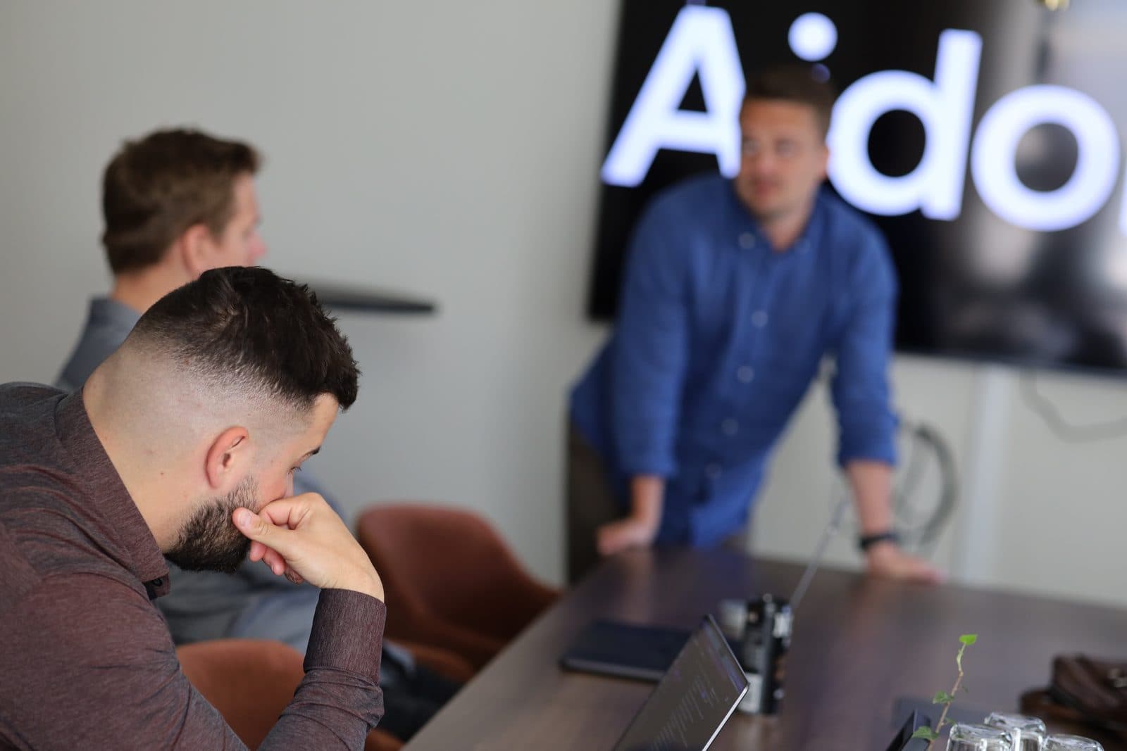 Aidoni-kollegor i ett möte, med Aidoni-loggan på skärmen
